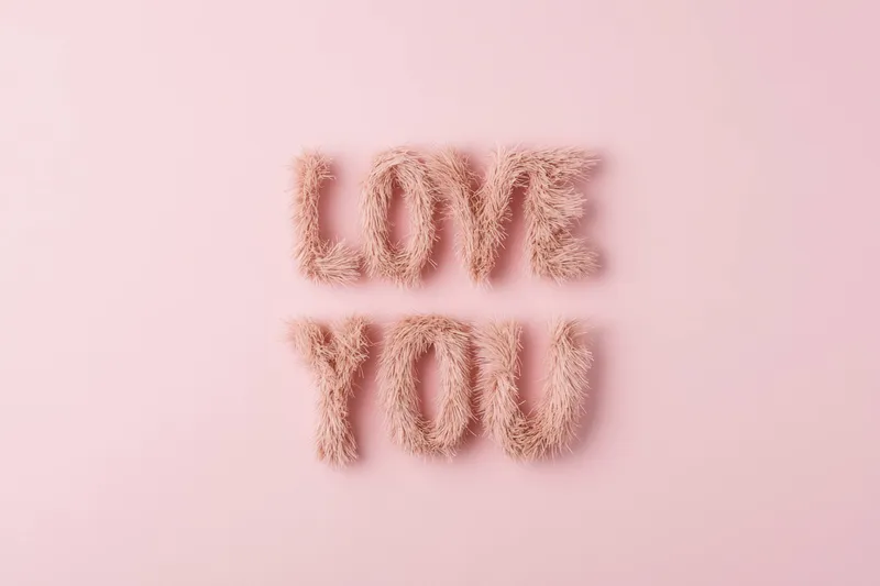 Это художественное изображение фразы LOVE YOU, выполненное из мягких розовых волокон на нежном розовом фоне