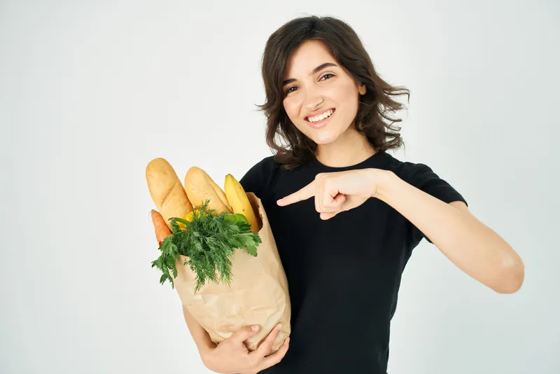 Веселая брюнетка с пакетом продуктов из супермаркета здорового питания