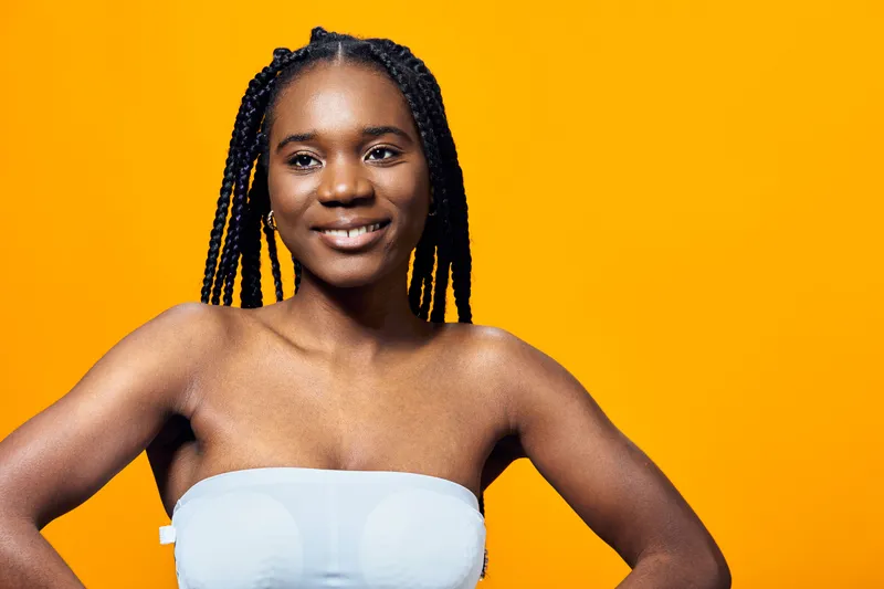 Smiling Black woman with braided hair against a bright yellow background, showcasing confidence and beauty in summer fashion