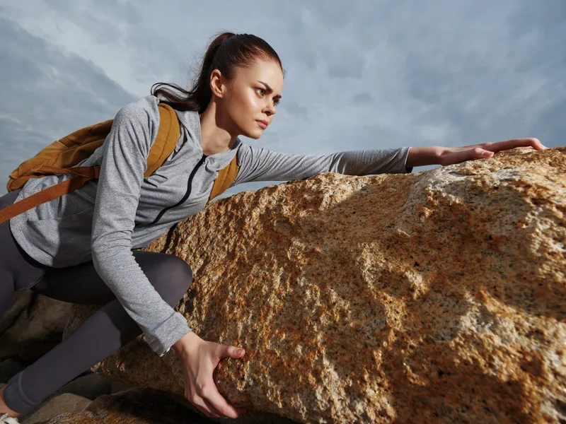 Determined female hiker in activewear overcoming rocky terrain, showcasing resilience and strength with a stunning natural backdrop