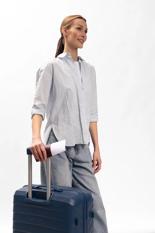 Young woman with suitcase standing isolated on white background, wearing casual clothes and looking away. Concept of travel, tourism, vacation, and lifestyle with luggage and preparation.