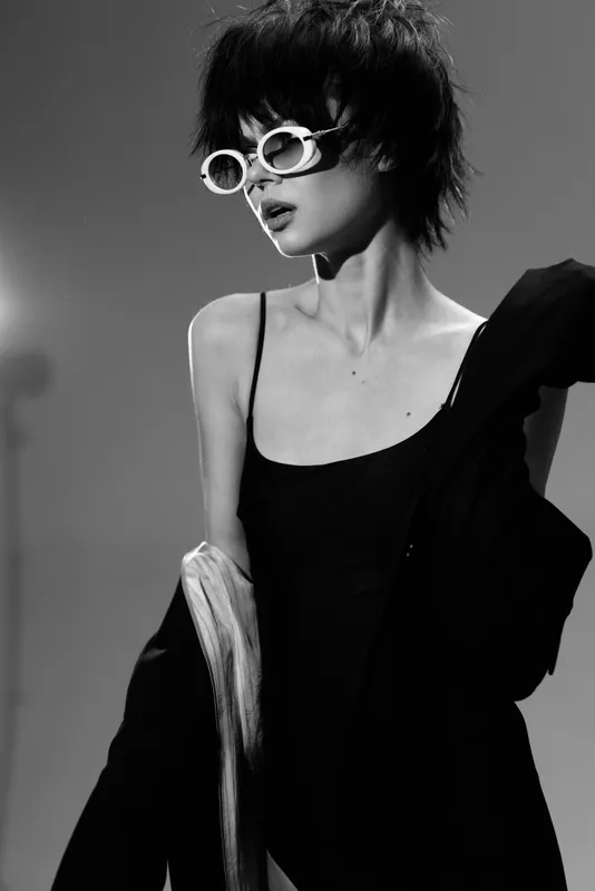 Stylish woman wearing white sunglasses in black and white minimalist fashion portrait with short hair and confident expression.