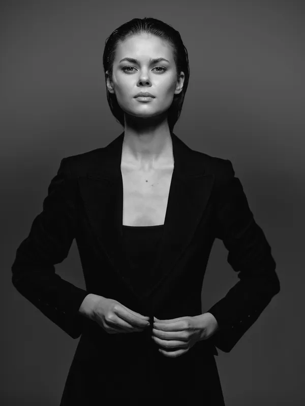 Black and white portrait of confident woman in dark blazer with serious expression and studio lighting.