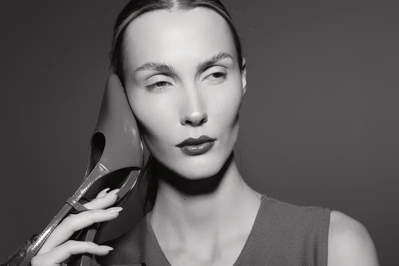 Portrait of a slender white woman holding a high heel shoe near her face. Concept of fashion, elegance, and artistic black and white photography.