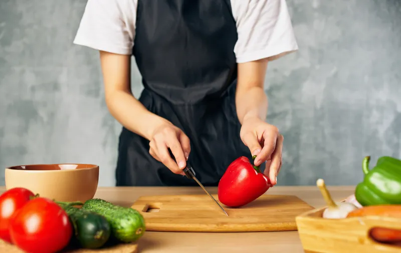 Женщина в черном фартуке нарезает овощи, кухня, приготовление еды, свежие продукты