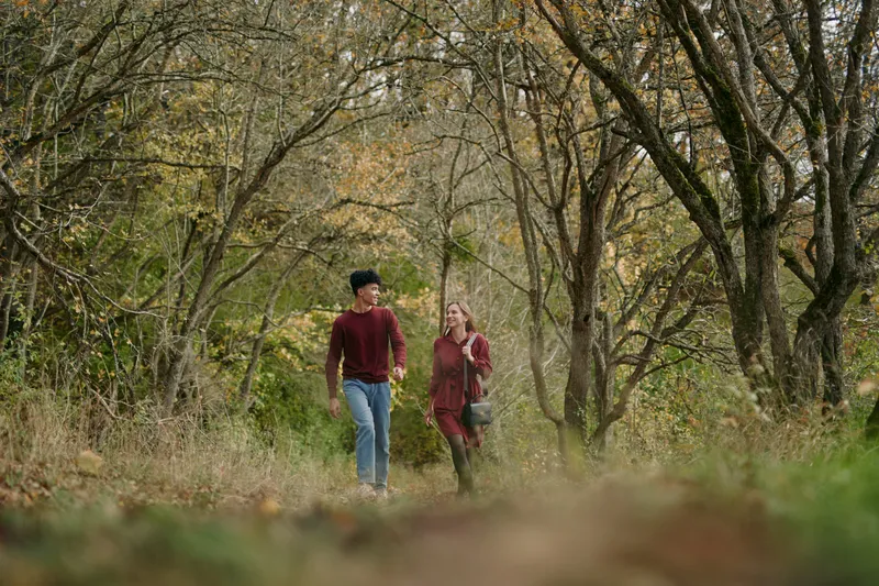 Authentic moment of two hikers strolling along a quiet forest path, capturing genuine connection and natural simplicity amid autumn light and a gentle breeze.