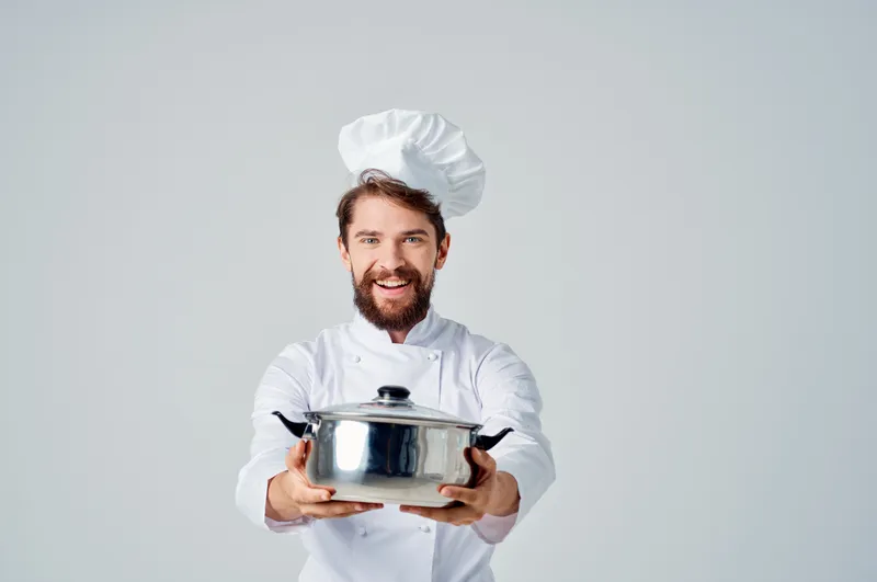Весёлый повар с кастрюлей в руках на кухне, приготовление еды, светлый фон