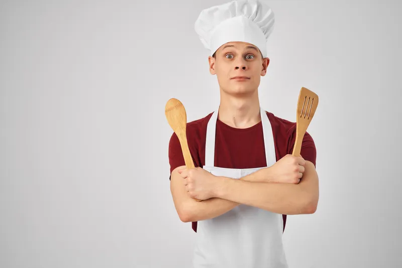 Повар-мужчина в белом фартуке и с кухонной утварью готовит в ресторане