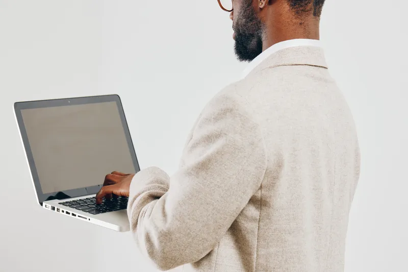 Professional man working on laptop with a neutral background, dressed in beige blazer, focused and engaged. Studio shot capturing technology use and concentration, suitable for business, remote work, 