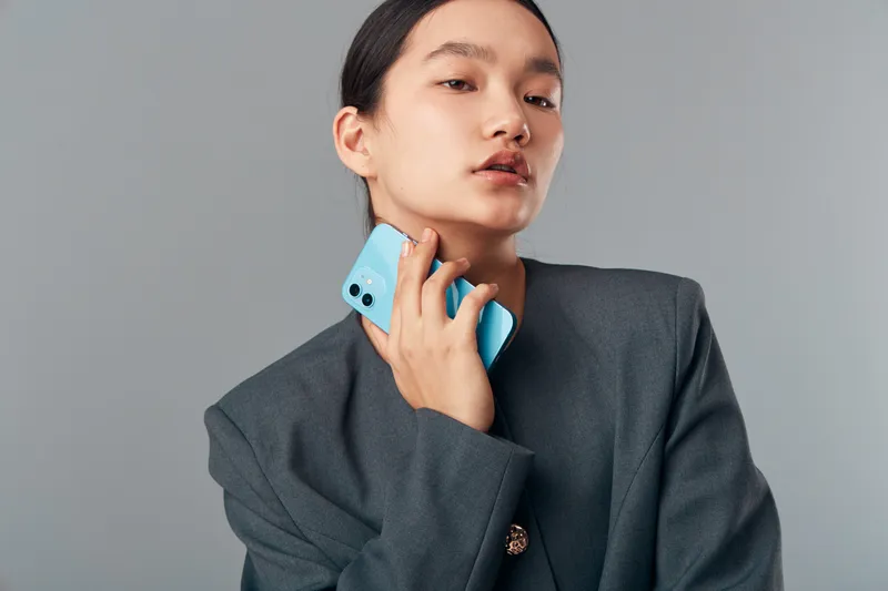 Woman, smartphone, portrait and casual with confident expression wearing oversized blazer posing against gray wall. Technology, fashion and lifestyle with modern communication and style.