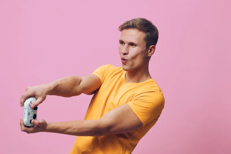 Young man taking a selfie with a smartphone, wearing casual yellow t-shirt, standing against pink background, capturing cheerful moments, lifestyle concept, social media, technology, fun, youth.