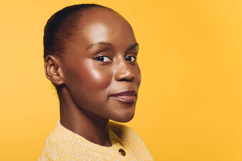Confident African woman with dark skin and natural makeup looks at camera against yellow background. Concept of beauty, self-confidence, and healthy skin care for black women.