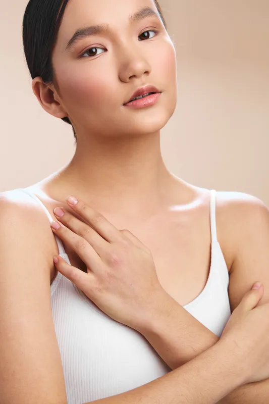 asian woman portrait in soft lighting with a calm expression, delicate smile, and relaxed posture, wearing a white top, conveying elegance and serene confidence.