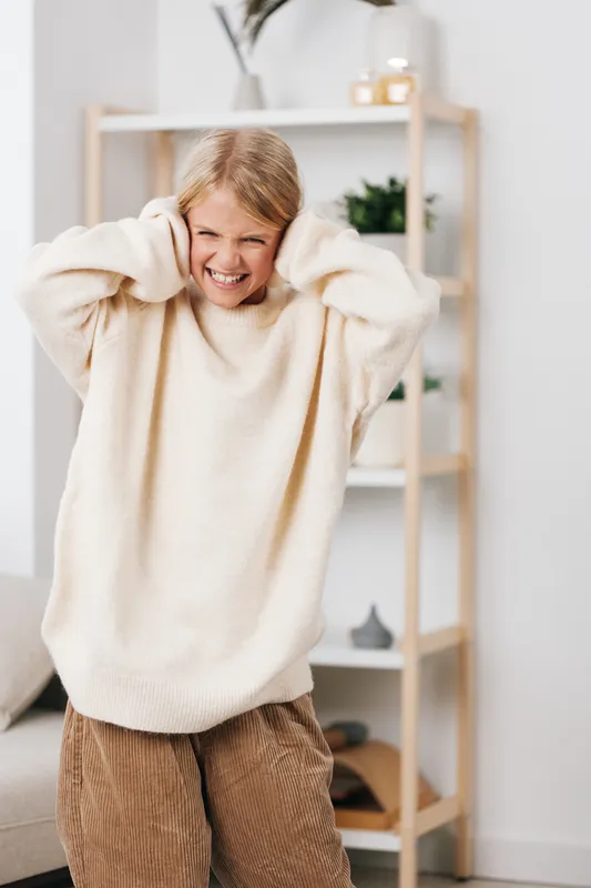 An authentic lifestyle image of a student at home, wearing a cozy sweater, capturing a candid moment of playful focus that conveys everyday school life and genuine mood.