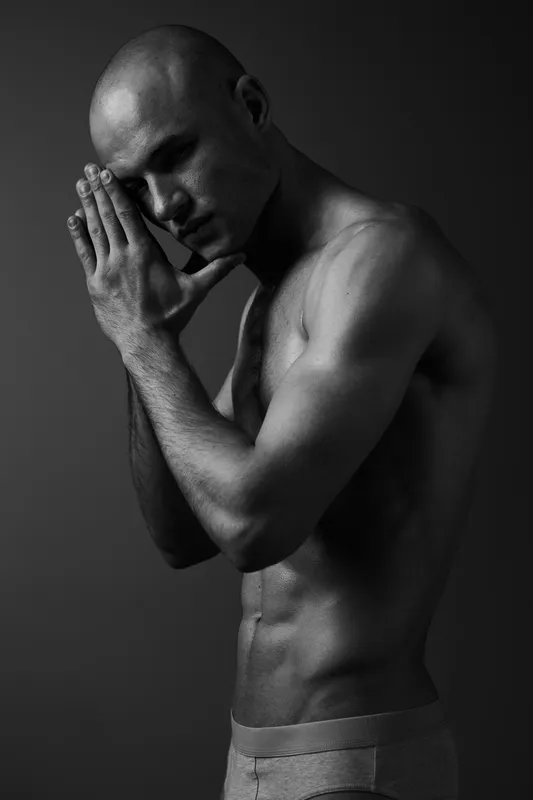 Black and white portrait of a contemplative man, showcasing strong emotion and artistry, emphasizing the contrast of light and shadow in striking details.