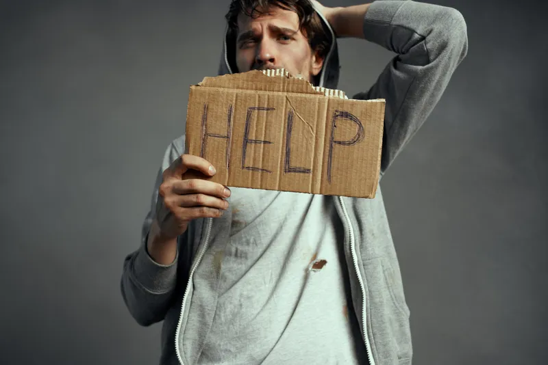 Бедный бродяга держит табличку с надписью «Help» на улице