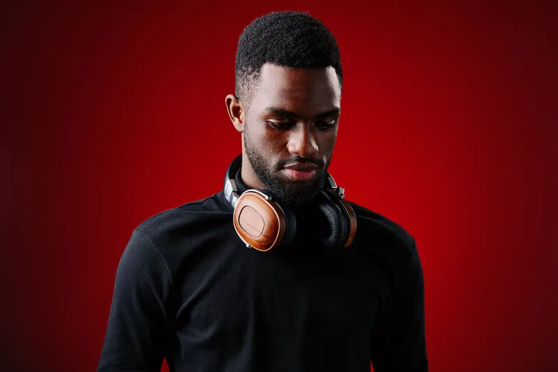 Young African man with headphones on his neck, wearing a black shirt, with a contemplative expression against a red background