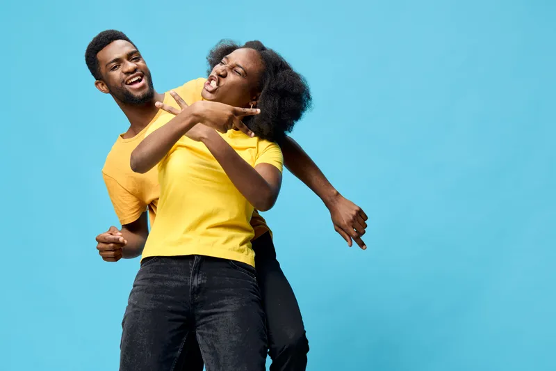 Happy young African couple having fun against a bright blue background, wearing yellow t shirts, expressing joy and energy Key themes include love, friendship, and vibrant colors
