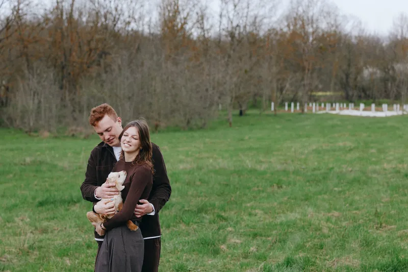 Happy couple in a park embrace with a dog, enjoying outdoors, casual lifestyle, warm affection, and vibrant autumn scenery. with gentle breeze and natural light, capturing joyful moment.