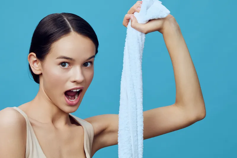Young woman with a towel expressing surprise against a blue background, showcasing vibrant emotions and a fresh, clean aesthetic
