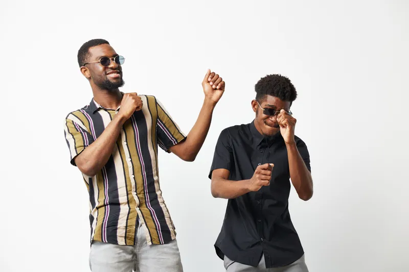 Joyful black men dancing together in stylish sunglasses, showcasing friendship and celebration. Their vibrant attire adds energy to the fun atmosphere.