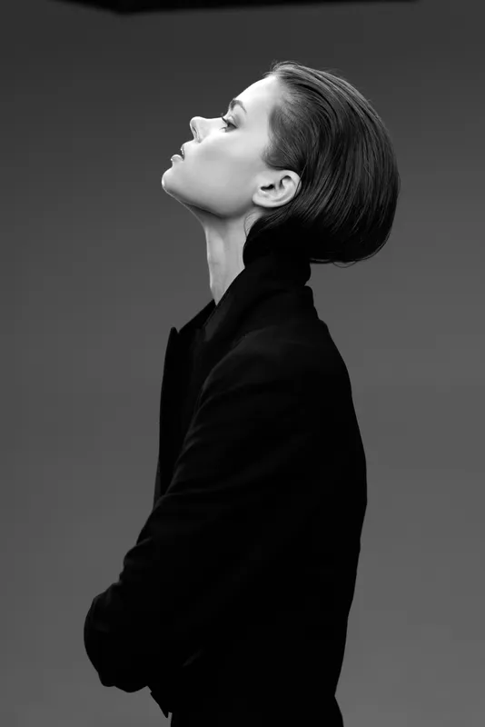Black and white portrait of a woman in profile with closed eyes wearing a dark coat, conveying elegance and calmness.
