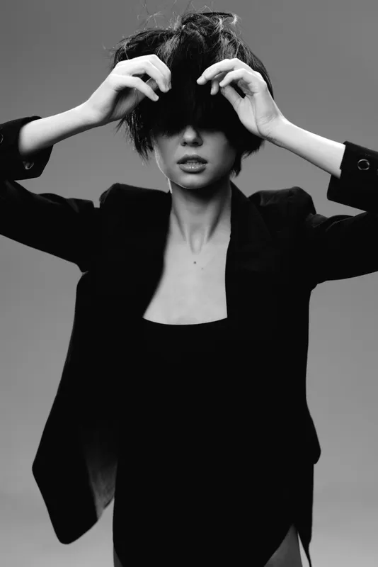 Black and white portrait of a stylish woman in a blazer with messy hair covering her eyes, expressing mystery and fashion elegance.