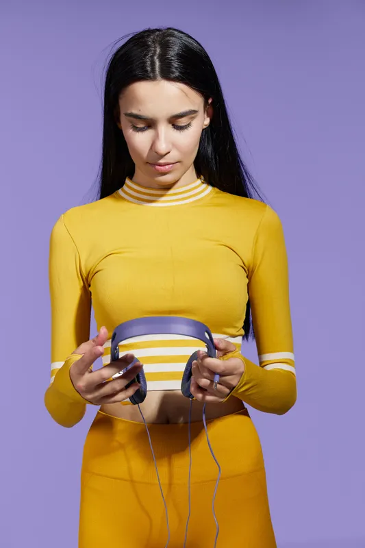 Young woman sport fitness preparing headphones, dressed in yellow activewear, focused and calm, isolated on purple background, healthy lifestyle concept.