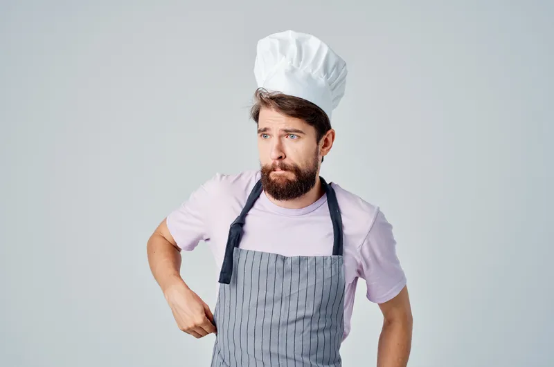 Эмоциональный бородатый мужчина в фартуке работает на кухне, предоставляя услуги