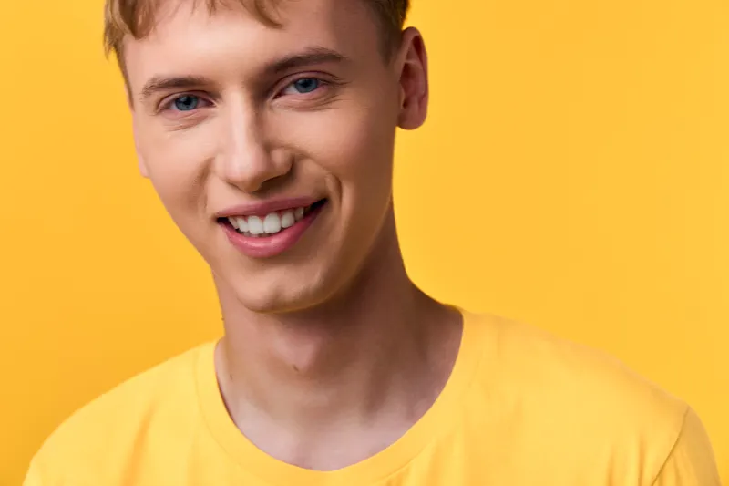 Smiling man in a yellow shirt against a bright yellow background, conveying warmth, cheerfulness, and friendly energy for lifestyle, fashion, or summer themed campaigns