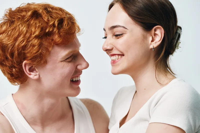 Young couple smiling and looking at each other with affection in a bright studio setting. Man and woman expressing happiness and close connection together.