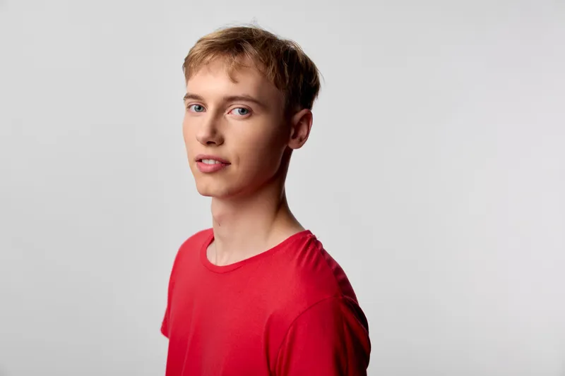 Young man in a red shirt against a plain backdrop, clean studio style, relaxed expression and soft lighting, suitable for fashion, lifestyle, or professional use in marketing and branding