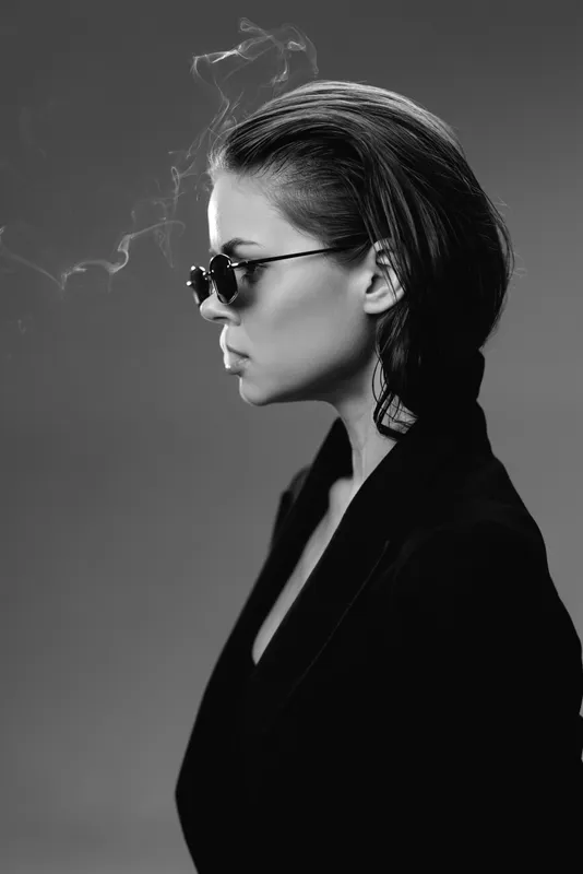 Black and white profile of a stylish woman with sunglasses smoking, wearing earrings and a dark jacket.