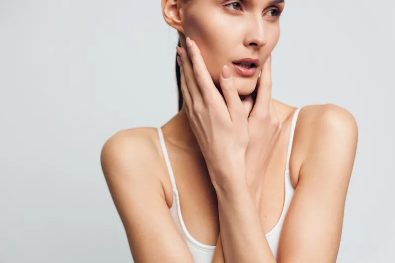 Woman portrait skincare beauty studio young healthy spa relaxing cosmetic concept, closeup female touching chin and cheek, bare shoulders, calm expression, white studio background, minimal aesthetic,