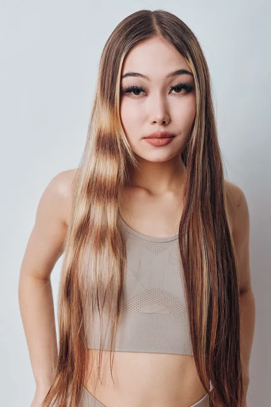 Portrait of young woman with long straight hair and tank top standing against plain background. Female model looking at camera with neutral expression in studio lighting.