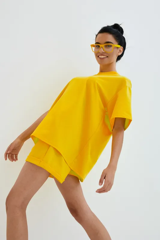 smiling woman in yellow casual outfit and matching glasses posing against white background, joyful expression, modern minimalistic style, bright color palette
