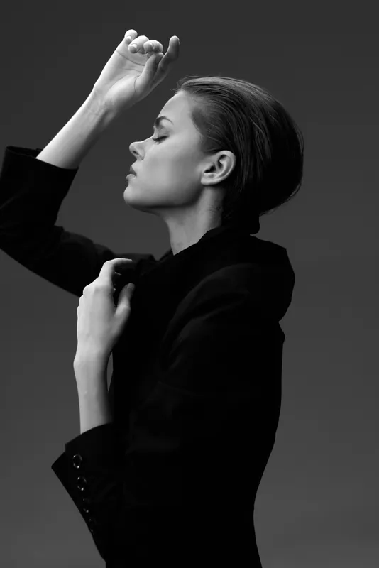 black and white portrait of a confident woman in a dark blazer with closed eyes and raised hand