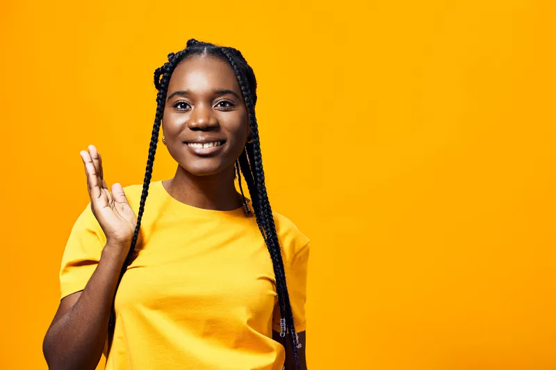 Smiling African woman in a yellow t shirt against an orange background, showcasing positivity and warmth, ideal for concepts of friendship and well being