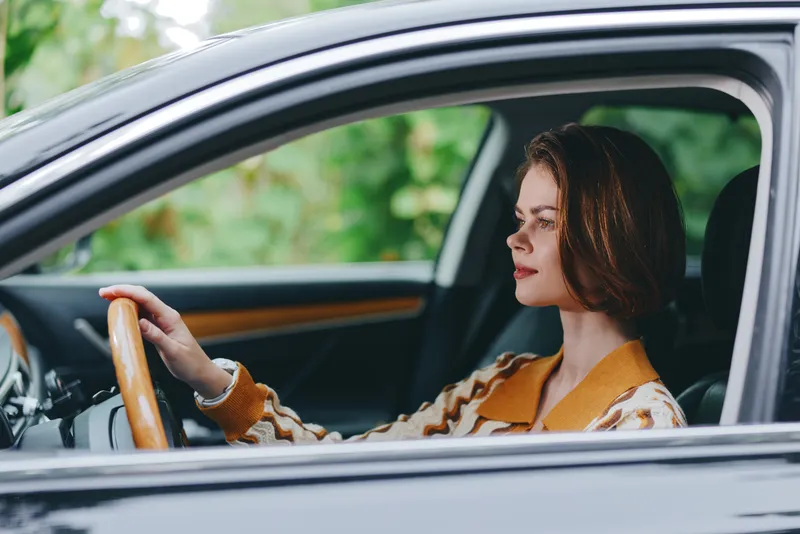 Portrait of a woman driving a car, focused and calm, bathed in warm natural light with a vintage interior and stylish mood.