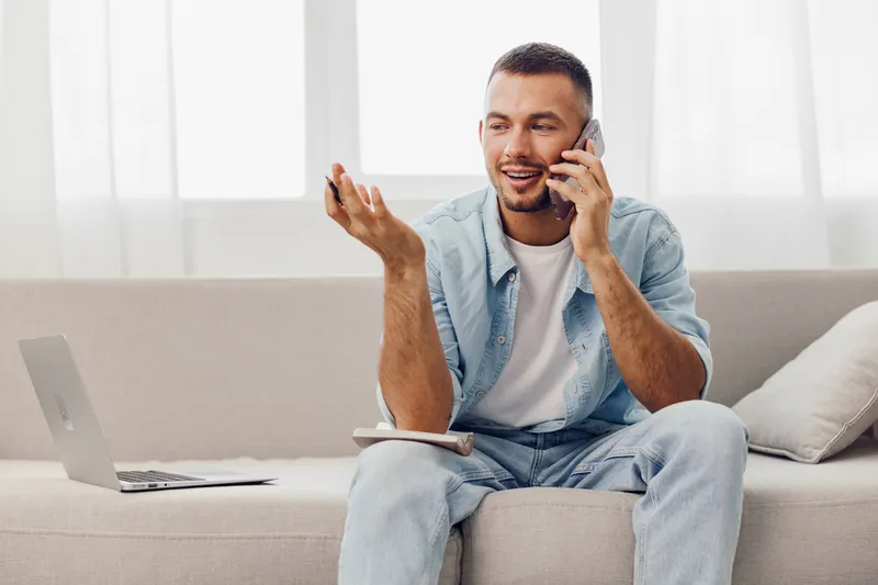 Smiling man on the phone, casual attire, relaxed setting, engaging conversation, modern workspace, natural light enhancing the ambiance.
