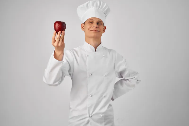 Шеф-повар с яблоком в руке, свежие продукты на профессиональной кухне