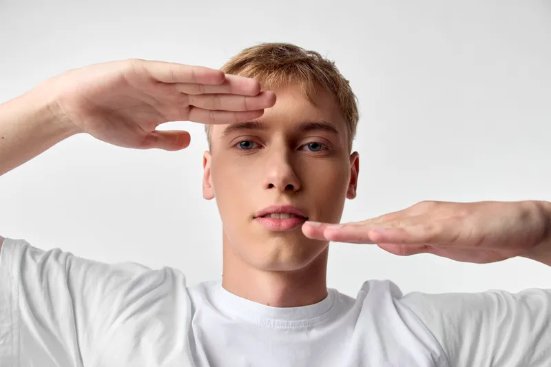 Framing technique with hands around a young face, man in a white tee, studio lighting, focus on composition, balance and angles for photography concept and framing practice