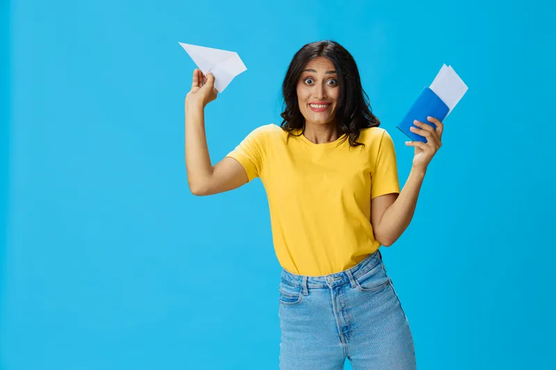 Женщина-путешественница с желтым чемоданом, паспортом и билетом в руках, бумажный самолетик, в желтой футболке на синем фоне, счастье от путешествия, очки, есть место для копирования
