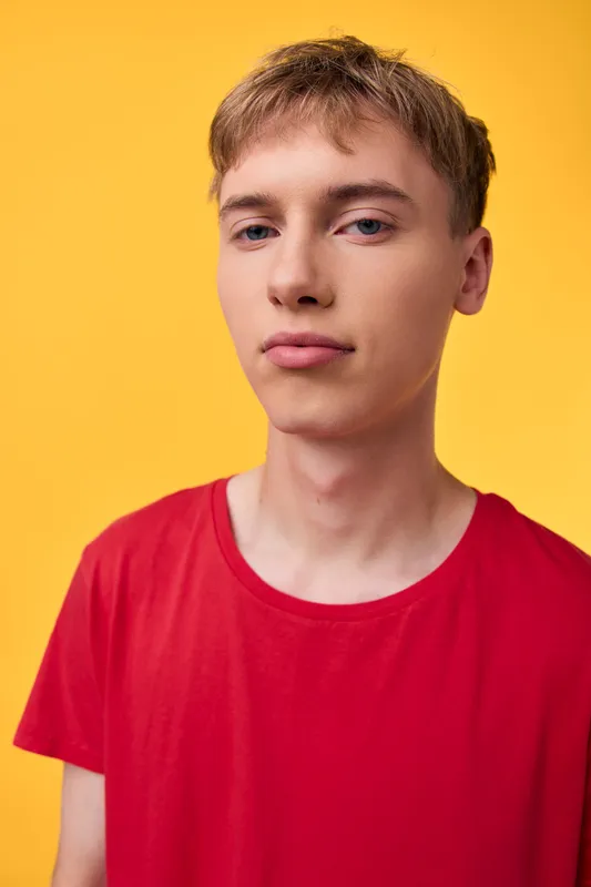Young man in a red shirt against an orange background, studio shot with casual style, clean lighting and neutral expression, ideal for fashion and lifestyle projects
