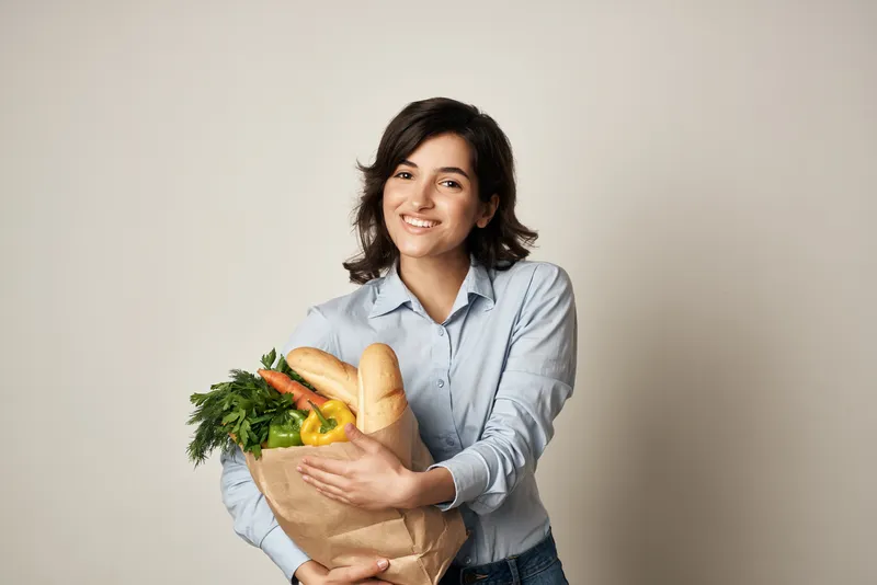 Брюнетка с пакетом продуктов из супермаркета, доставка диетического питания на тёмном фоне