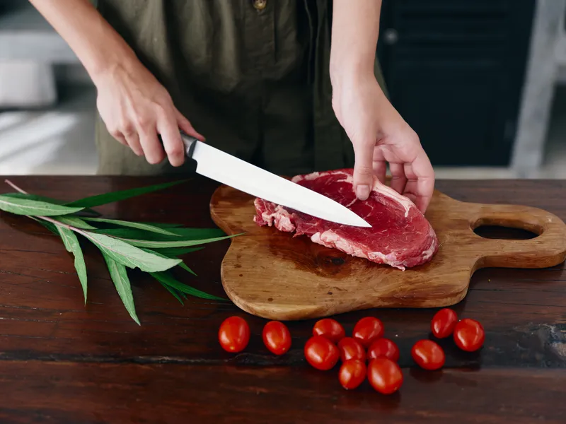 Женщина с ножом в руке нарезает свежее мясо для жарки на кухне