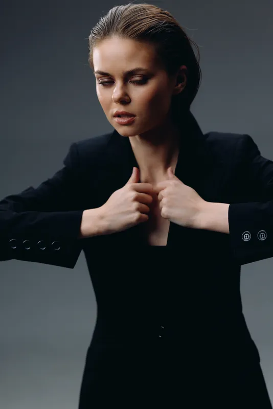 Young woman in black blazer with closed eyes, thoughtful expression, minimalist dark background, professional fashion style