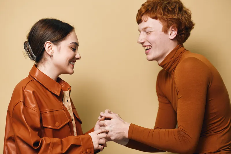 Young man and woman holding hands smiling with happy expressions in casual clothes on beige background for friendship and connection concept.
