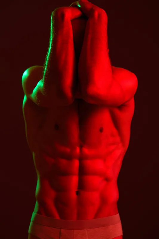 Male model showcasing strong physique under dramatic lighting with vibrant red and green tones. Capturing the intensity and emotion in a captivating black and white style.
