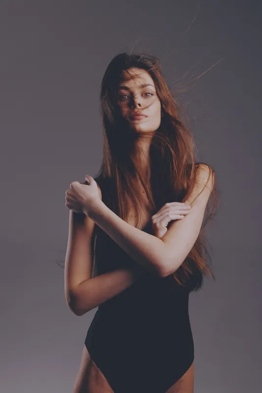 Elegant woman in black bodysuit with long hair posing confidently in studio lighting